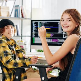 cheerful-pretty-teenage-girl-and-her-brother-smiling-at-camera-when-sitting-at-desk-and-doing-homework-for-computer-science-class